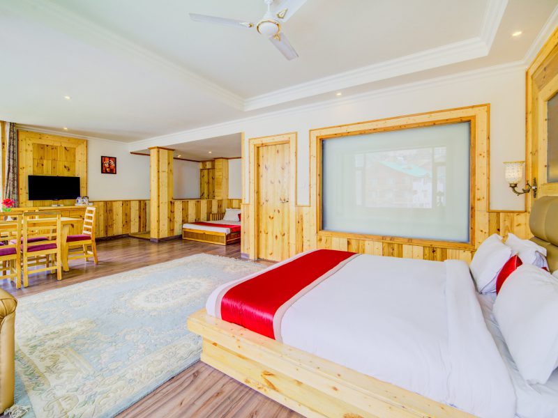 A well-appointed family suite at AHR Grace Resort showcasing a large bed, wooden interiors, and mountain views in Manali.