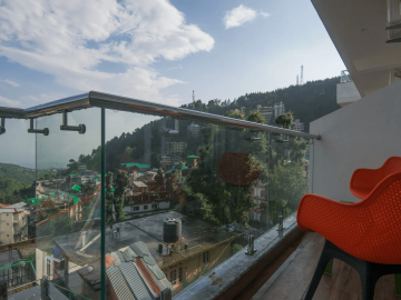 Scenic balcony with transparent balustrade and a red chair overlooking Dharamshala at AHR Shivaay Morex.